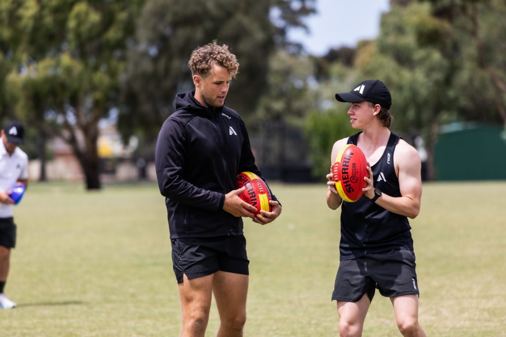 two Academy students holding AFL balls on a field